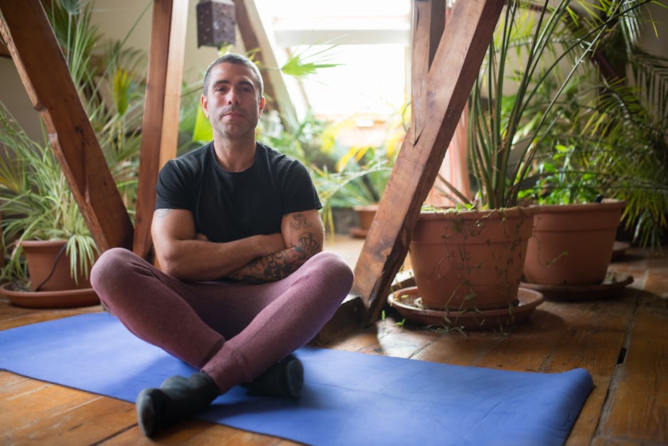 A smiling middle-aged man sitting cross-legged comfortably on a yoga mat